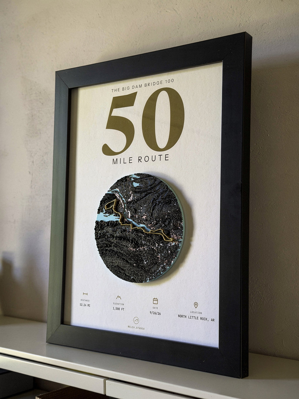 THE MARKER, 50 mile route of the Big Dam Bridge 100 — framed relief map viewed at an angle, showing the raised terrain and the brass route line