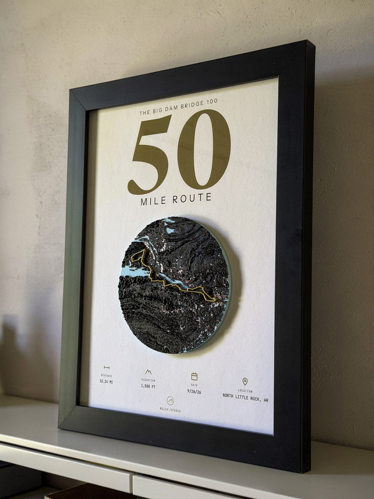 THE MARKER, 50 mile route of the Big Dam Bridge 100 — framed relief map viewed at an angle, showing the raised terrain and the brass route line